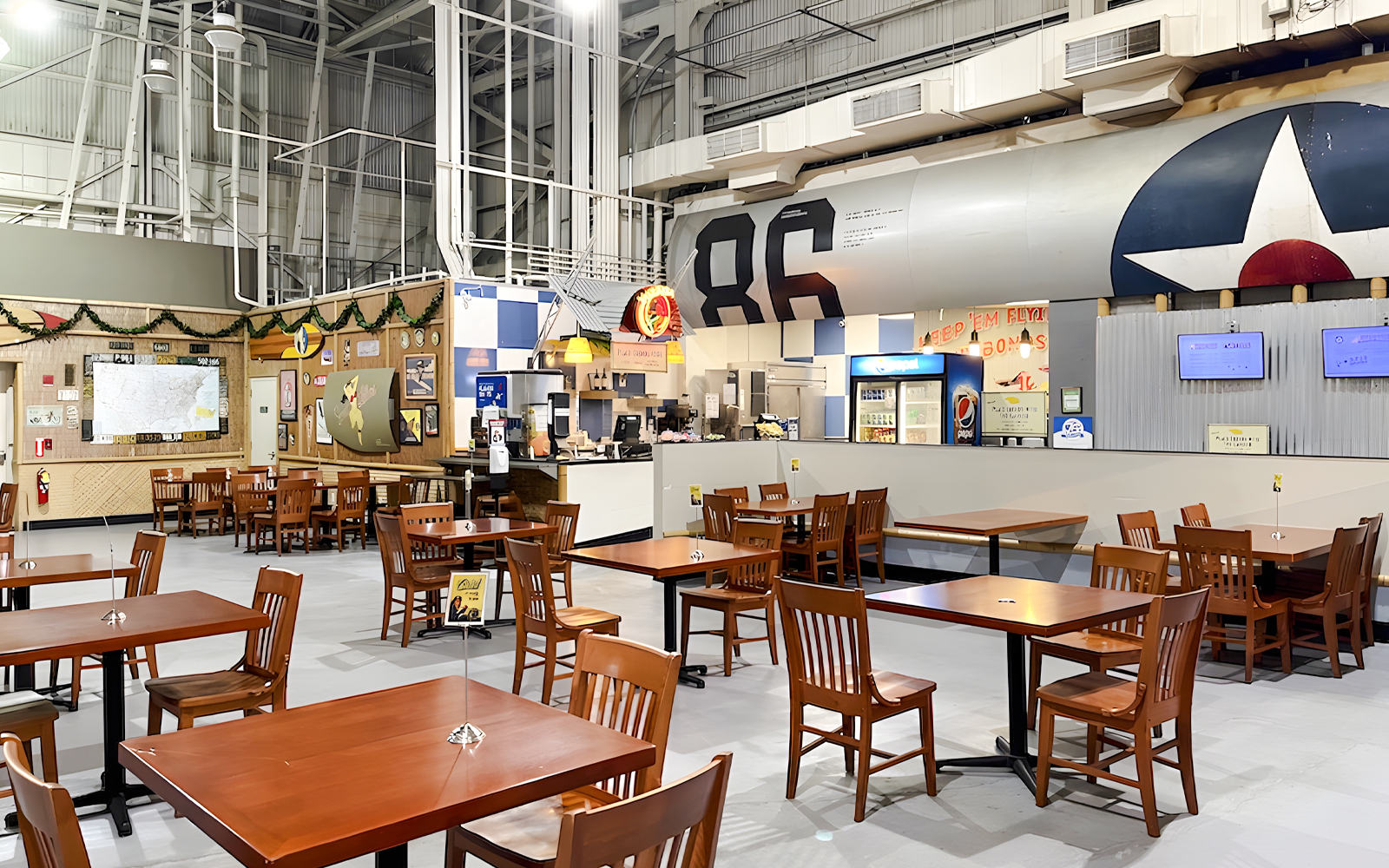 Cafe seating area inside Pearl Harbor Aviation Museum, featuring tables and a counter with aviation decor.