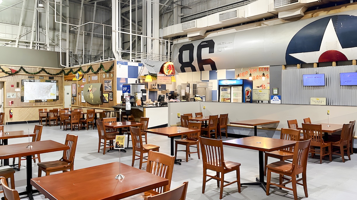 Cafe seating area inside Pearl Harbor Aviation Museum, featuring tables and a counter with aviation decor.
