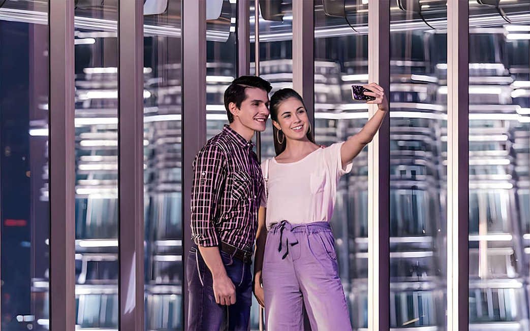 Couple taking a selfie inside a modern glass observation deck at night.
