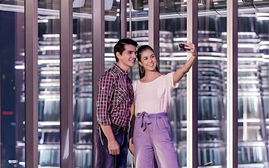 Couple taking a selfie inside a modern glass observation deck at night.