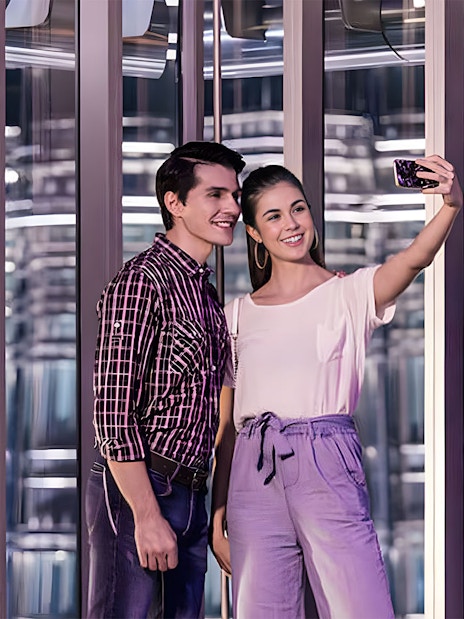 Couple taking a selfie inside a modern glass observation deck at night.