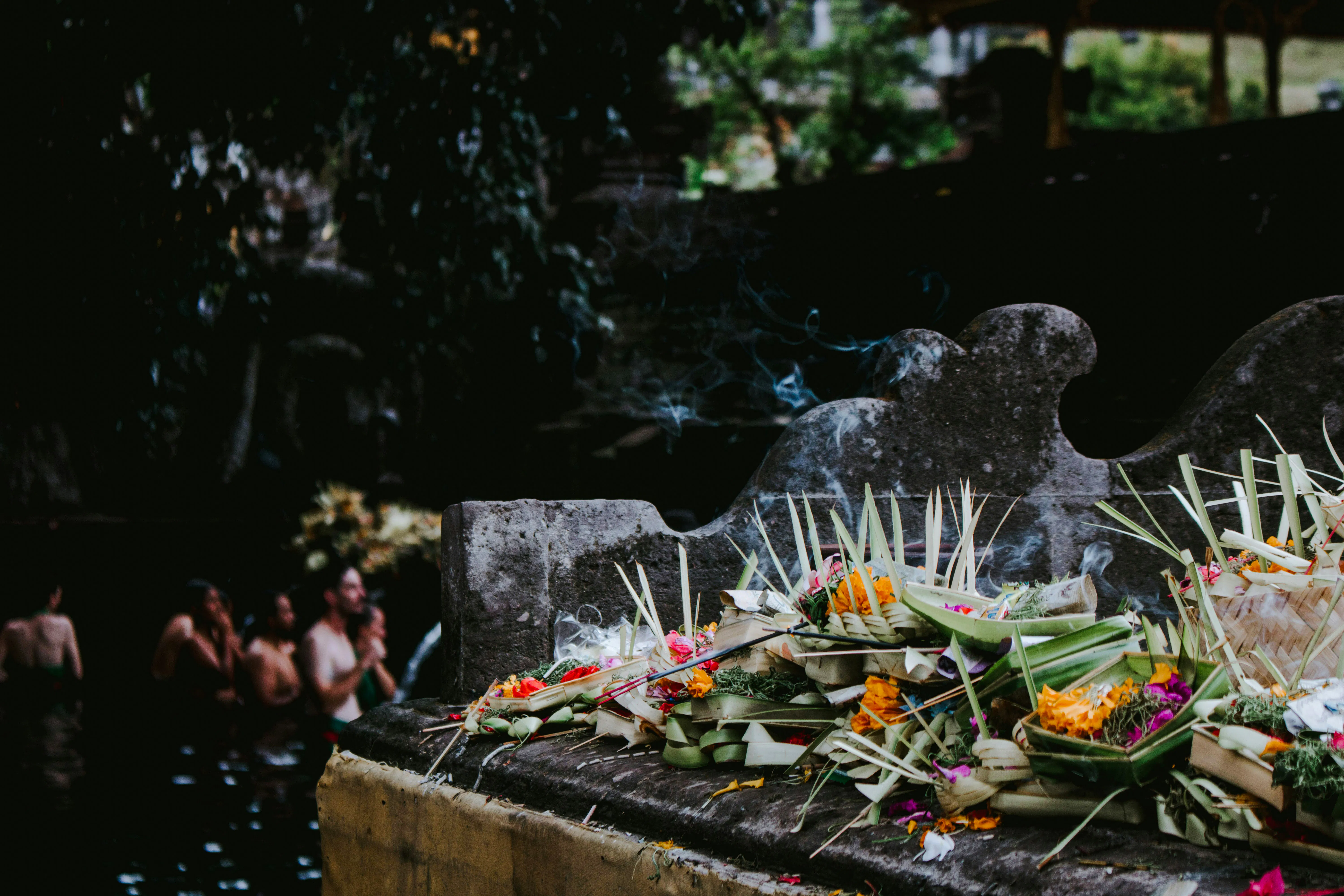 Offerings at Tirta Empul Temple with people in water, Bali.