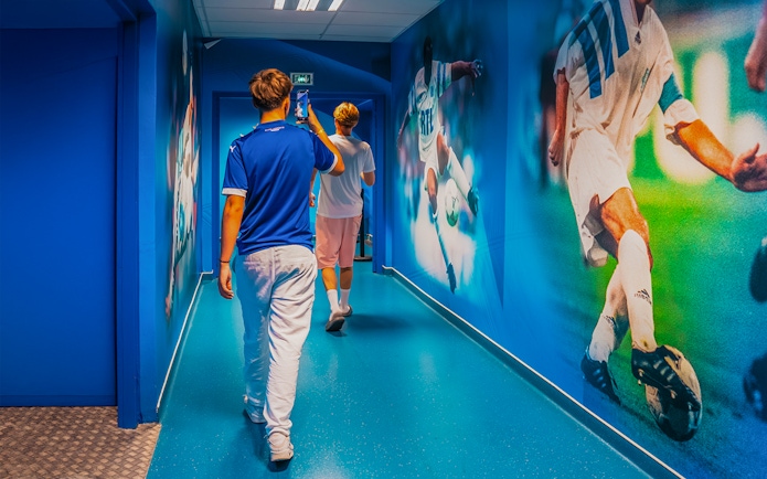 Visitors walking through OM Stadium hallway with football murals.