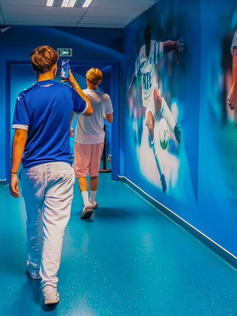 Visitors walking through OM Stadium hallway with football murals.