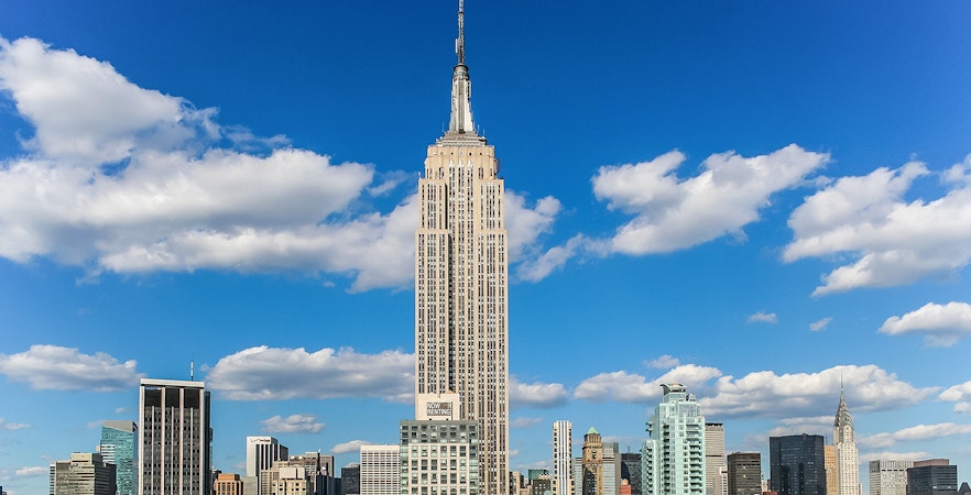 Empire State Building view from New York City street with yellow taxis and skyscrapers.
