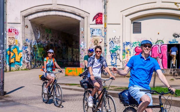 Cyclists on a guided tour ride past graffiti-covered walls in Berlin.