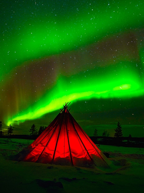 Northern Lights over snowy Rovaniemi landscape with illuminated tent during guided tour.
