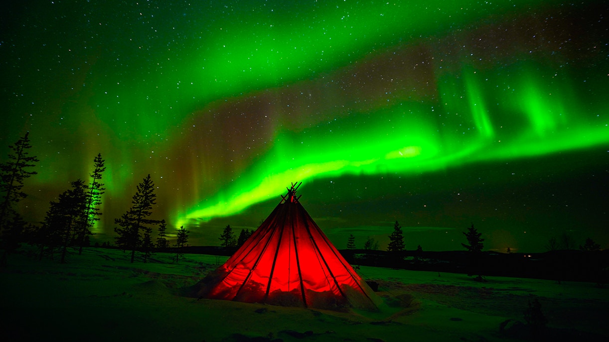 Northern Lights illuminating snowy landscape during guided tour with professional camera.