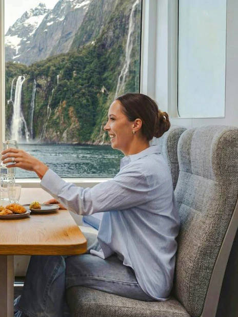 Couple enjoying a meal on a luxury cruise with Milford Sound waterfall view.
