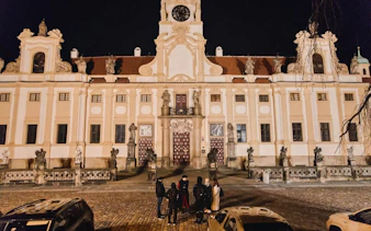 Group of tourists outside Prague Castle at night during guided tour.