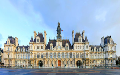 Hôtel de Ville facade in Paris with French flags and ornate architecture.