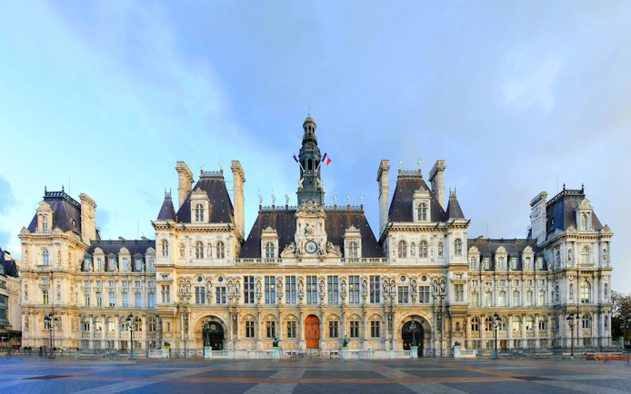 Hôtel de Ville facade in Paris with French flags and ornate architecture.