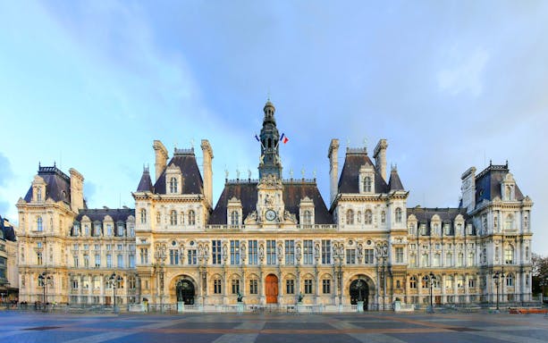 Hôtel de Ville facade in Paris with French flags and ornate architecture.