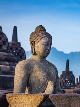 Buddha statue at Borobudur Temple, Java, Indonesia with stupas in the background.