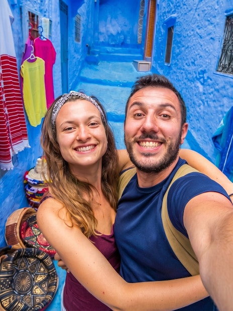 Couple taking a selfie in the vibrant blue streets of Chefchaouen, Morocco.