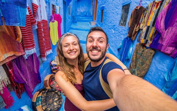 Couple taking a selfie in the vibrant blue streets of Chefchaouen, Morocco.