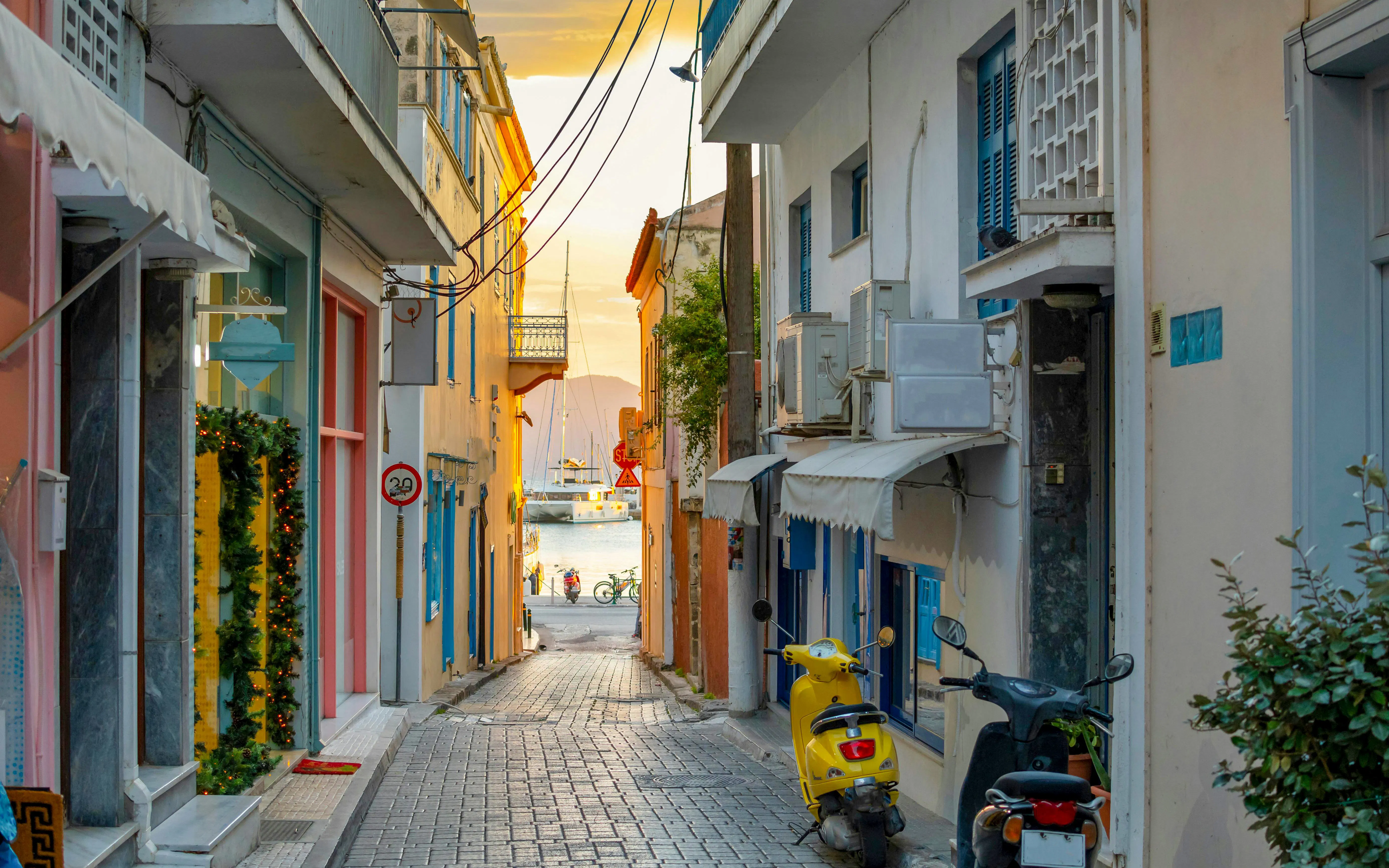 Narrow alleyway with colorful buildings and a yellow scooter on Aegina Island, Greece, leading to the sea.