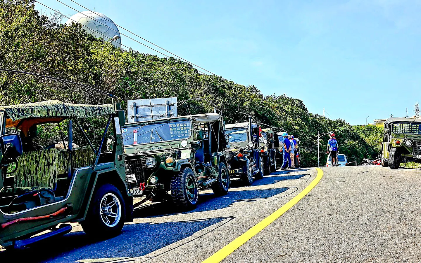 Jeeps lined up on Son Tra Peninsula road, Da Nang, with lush greenery and radar dome in background.