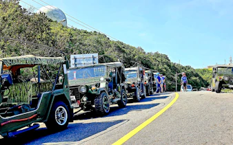 Jeeps lined up on Son Tra Peninsula road, Da Nang, with lush greenery and radar dome in background.