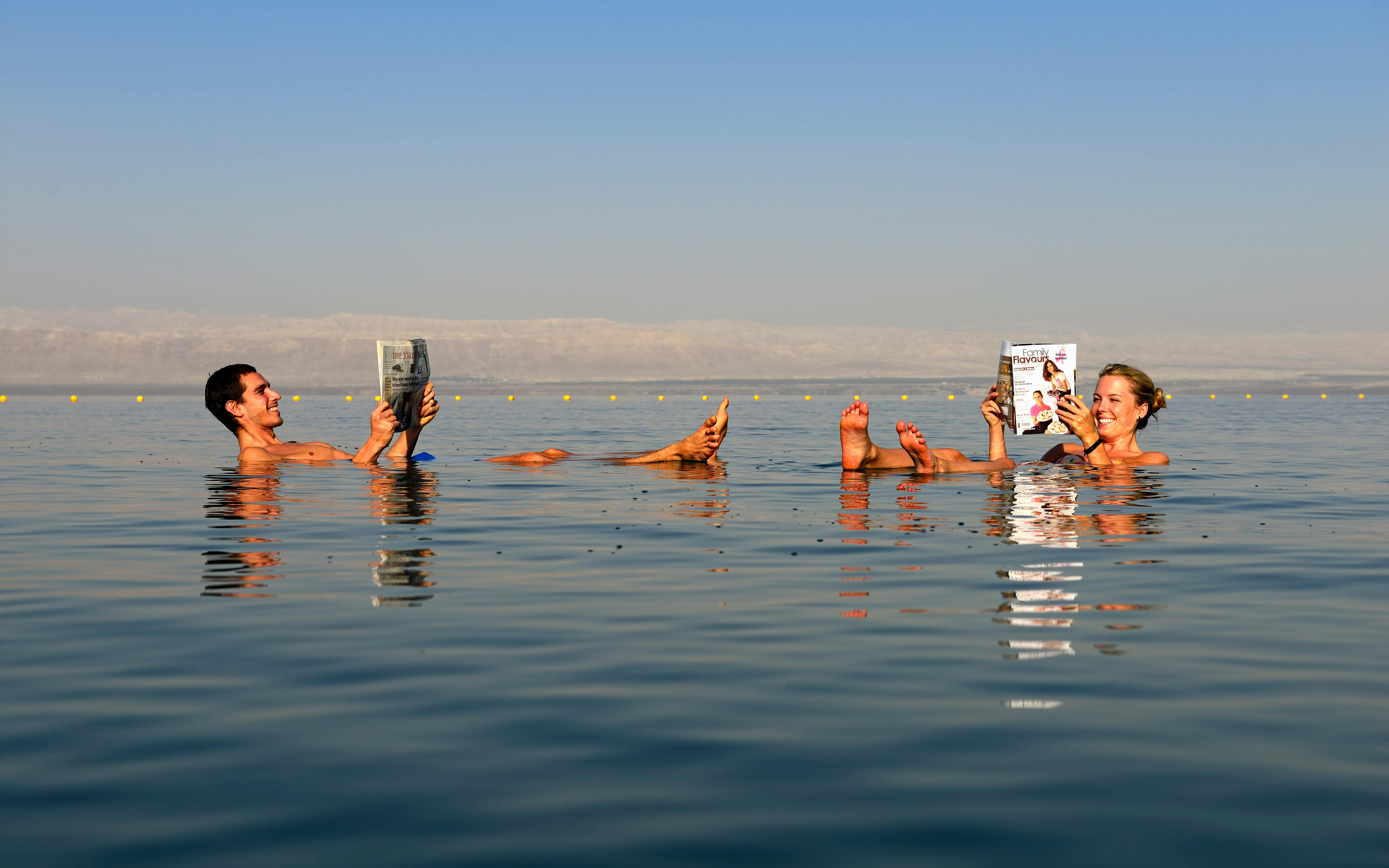 Couple reading while floating in the Dead Sea, Jordan.