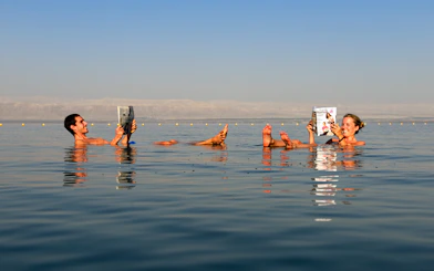 Couple reading while floating in the Dead Sea, Jordan.