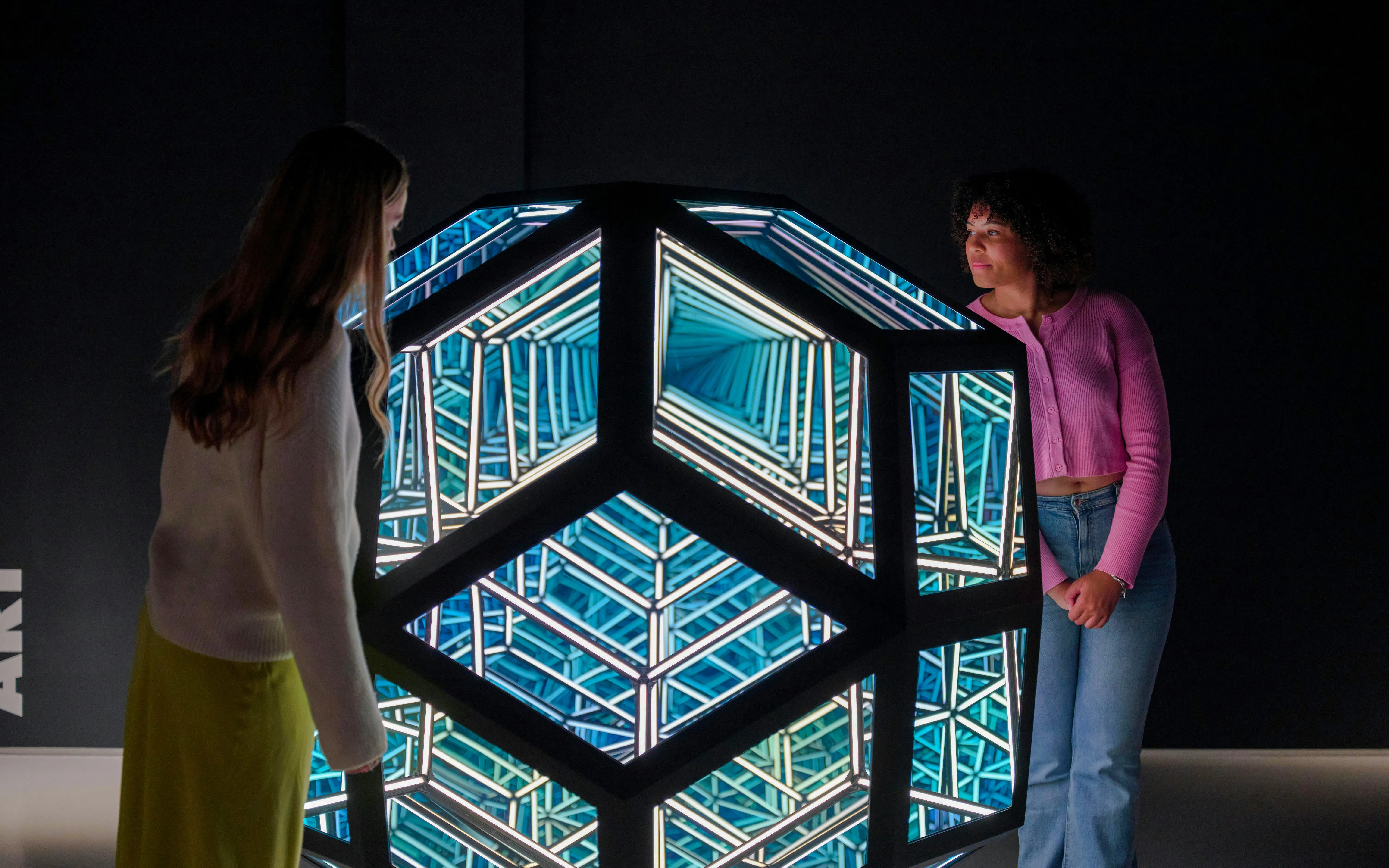 Visitors observing geometric light installation at Moco Museum, London.