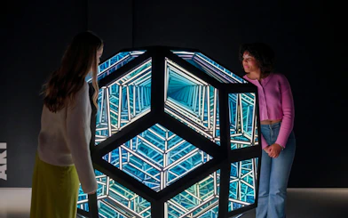 Visitors observing geometric light installation at Moco Museum, London.