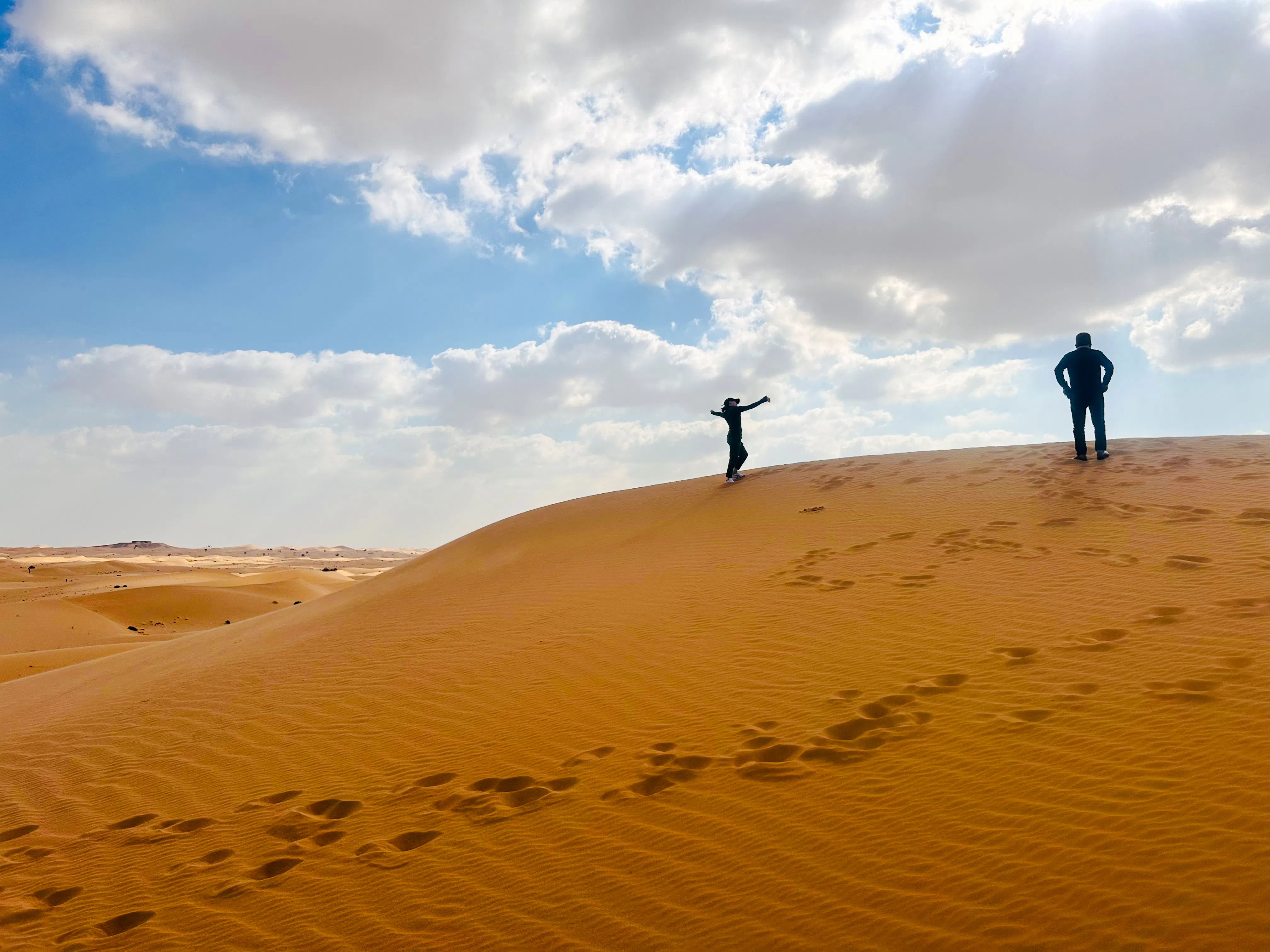 Two people standing on a sand dune during a sunrise desert safari in Abu Dhabi.