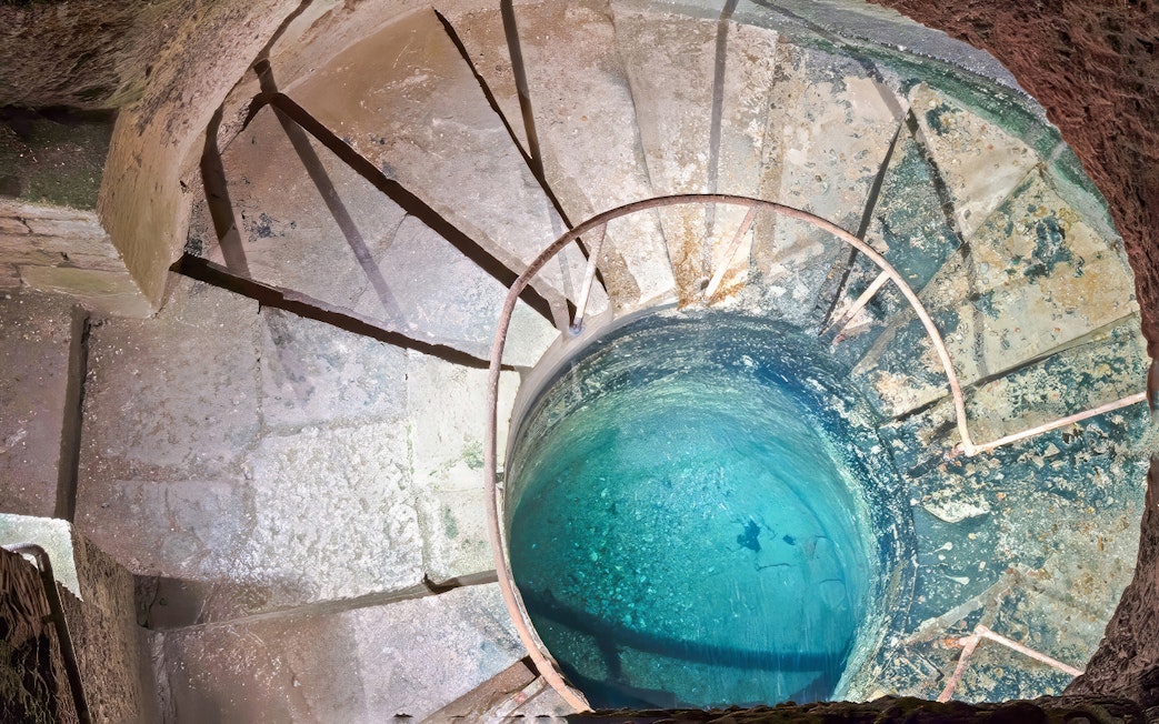 Quarrymen’s footbath in Catacombs’ Ossuary, Paris, with spiral stone steps and blue water.