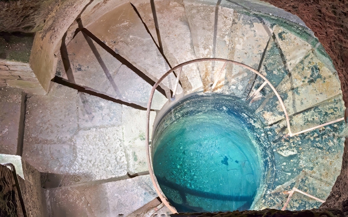 Quarrymen’s footbath in Catacombs’ Ossuary, Paris, with spiral stone steps and blue water.
