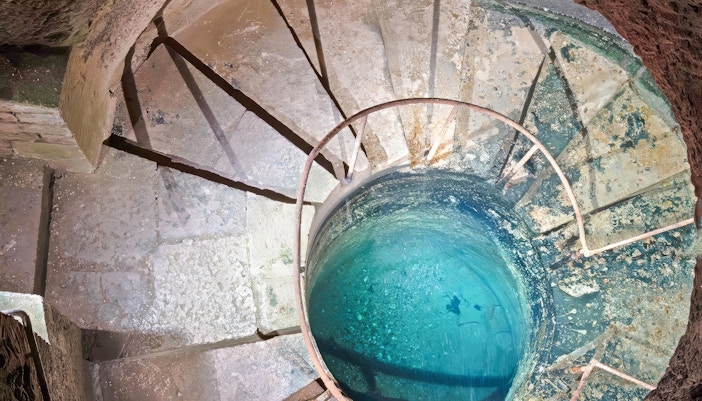 The underground well Catacombs, Paris, with spiral stone steps and blue water.