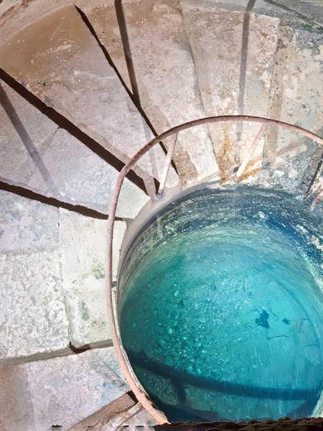 Quarrymen’s footbath in Catacombs’ Ossuary, Paris, with spiral stone steps and blue water.