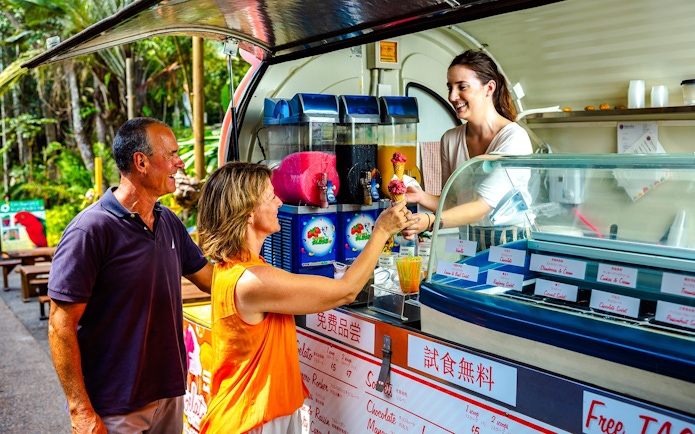 Tourists enjoying ice cream at a Kuranda market stall during the Scenic Train and Skyrail Kuranda Tour.