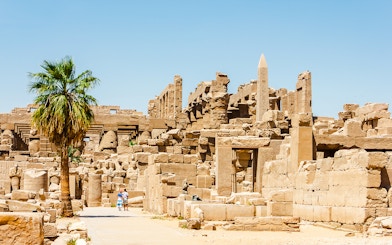 Luxor Temple ruins with palm tree and tourists exploring the ancient site.