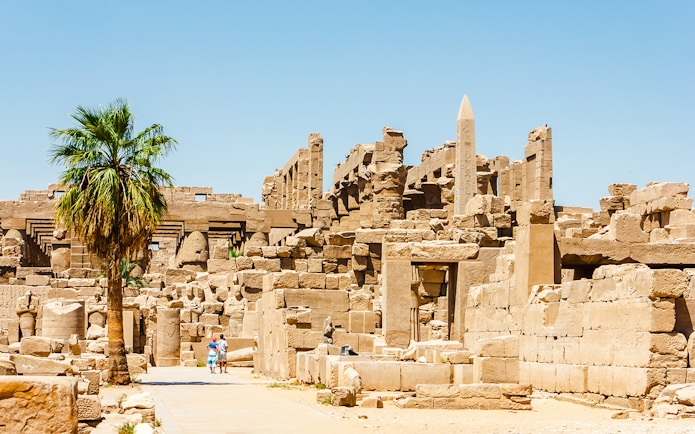 Luxor Temple ruins with palm tree and tourists exploring the ancient site.