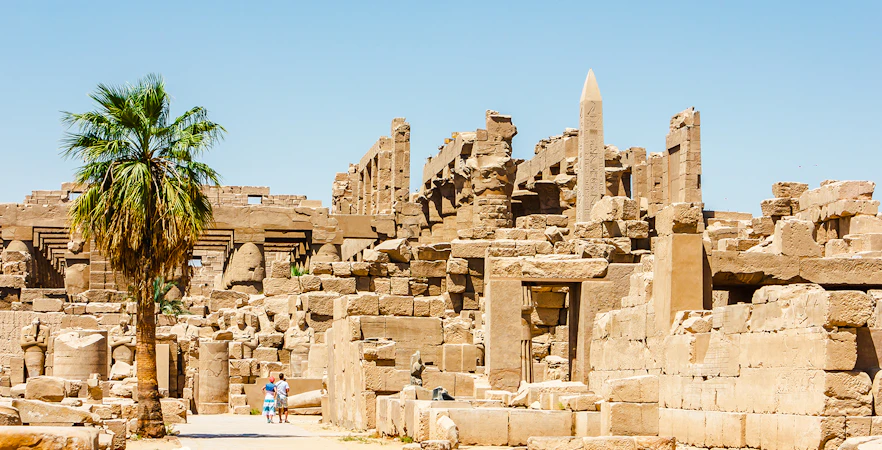 Luxor Temple ruins with palm tree and tourists exploring the ancient site.