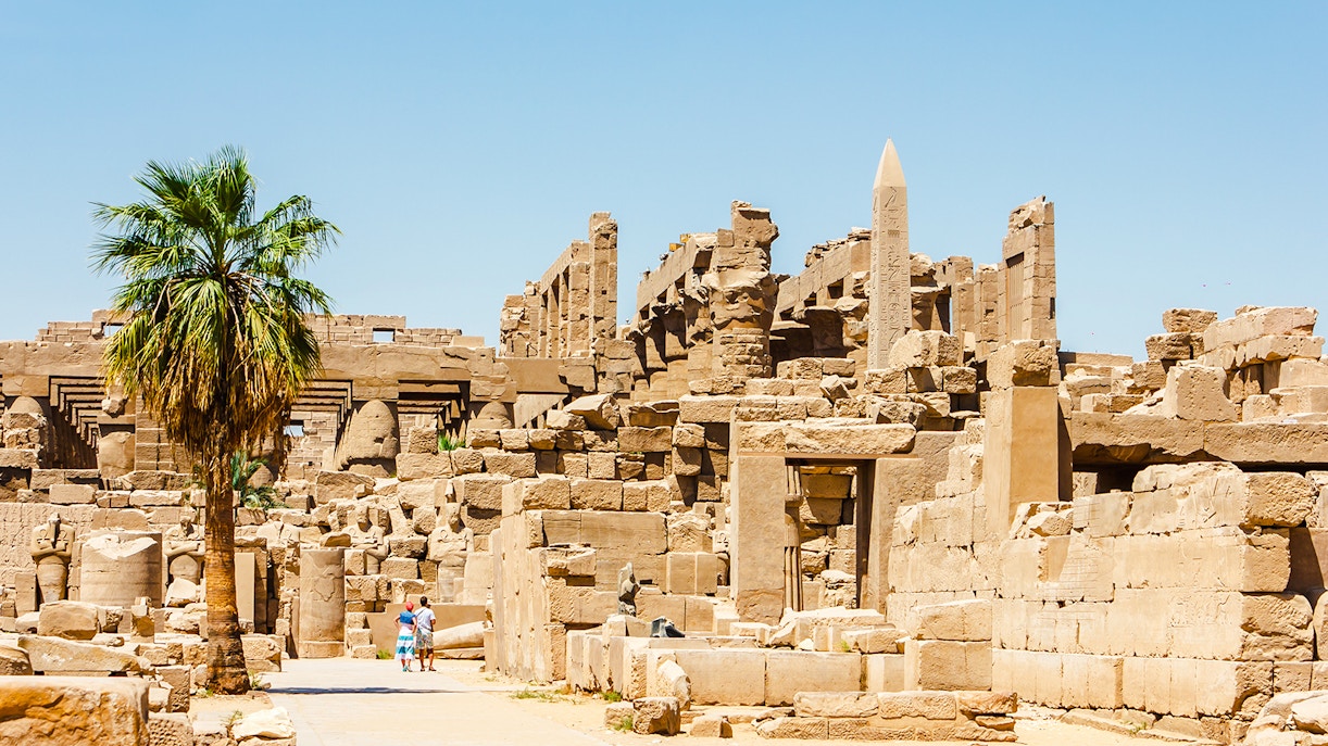 Luxor Temple ruins with palm tree and tourists exploring the ancient site.