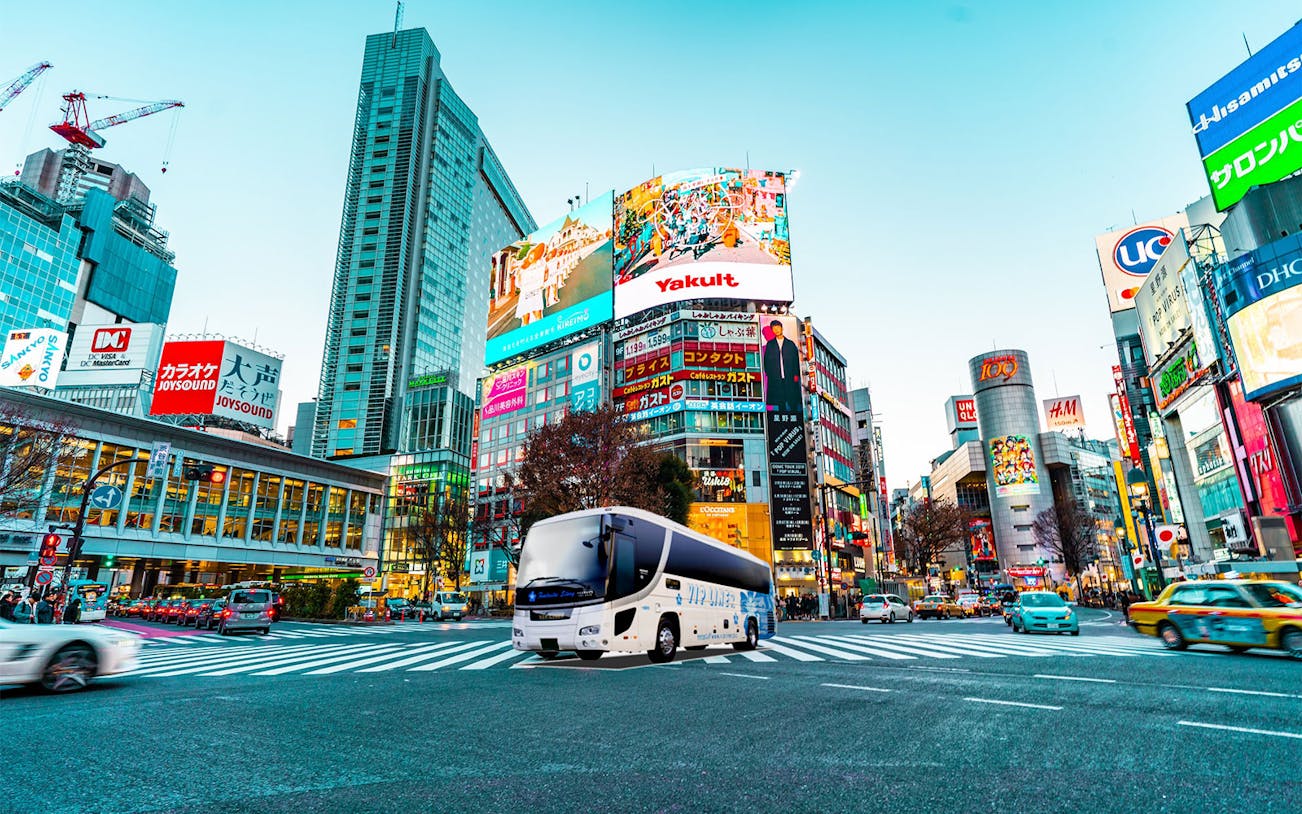 Overnight highway bus in Shibuya, Tokyo, with cityscape and billboards.