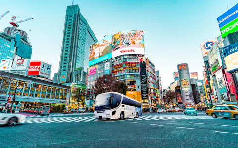 Overnight highway bus in Shibuya, Tokyo, with cityscape and billboards.