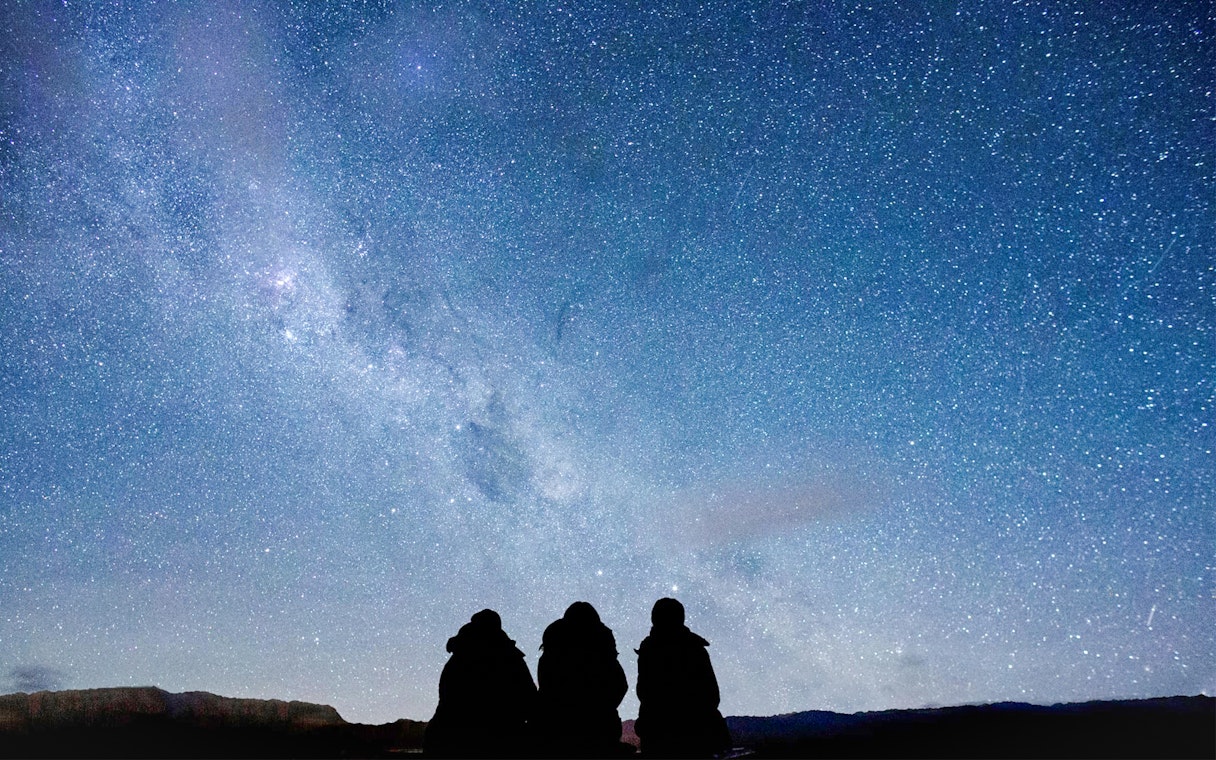 Silhouettes of guests stargazing at The Crater under a starry night sky.