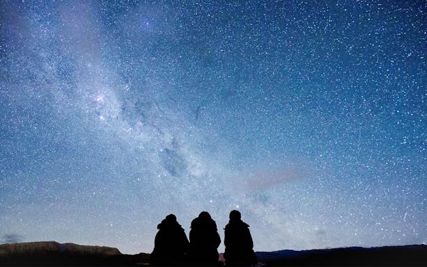 Silhouettes of guests stargazing at The Crater under a starry night sky.