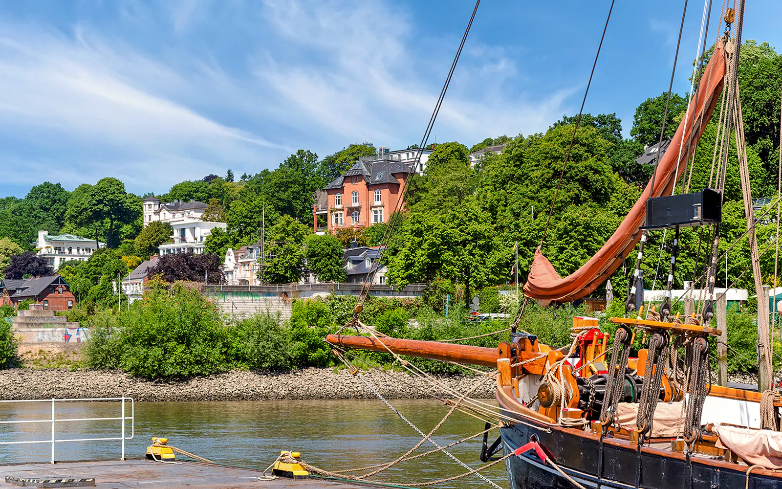 Sailing ship docked at Hamburg harbor with hillside houses in the background.