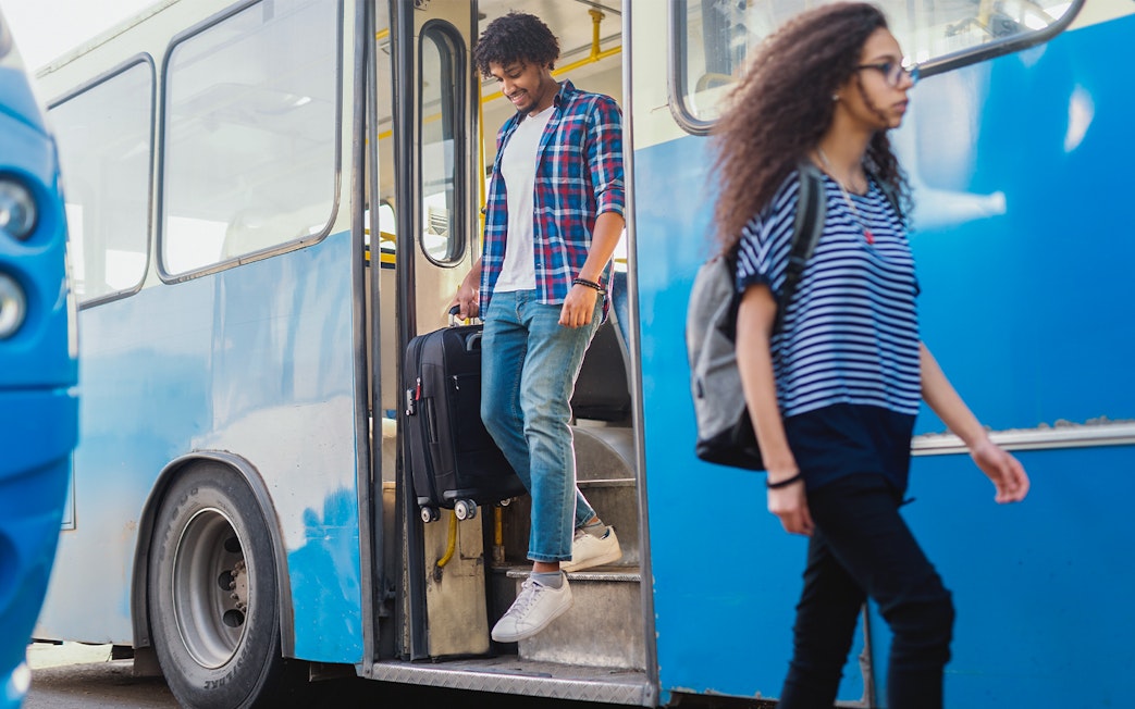 Man exiting bus with luggage in hand.