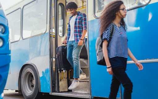 Man exiting bus with luggage in hand.