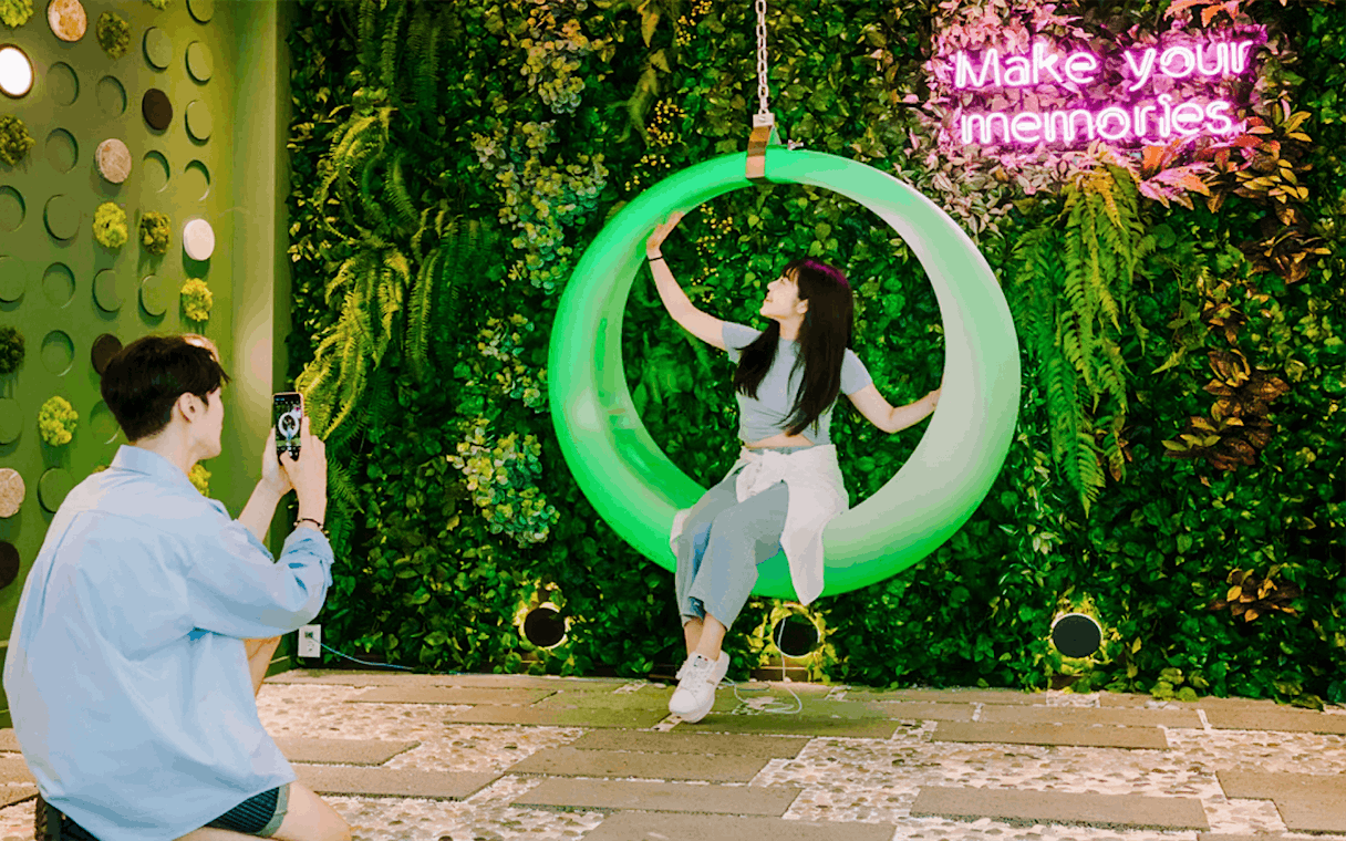 Couple enjoying Gangchon Gimnyujeong Rail Bike with neon sign backdrop.