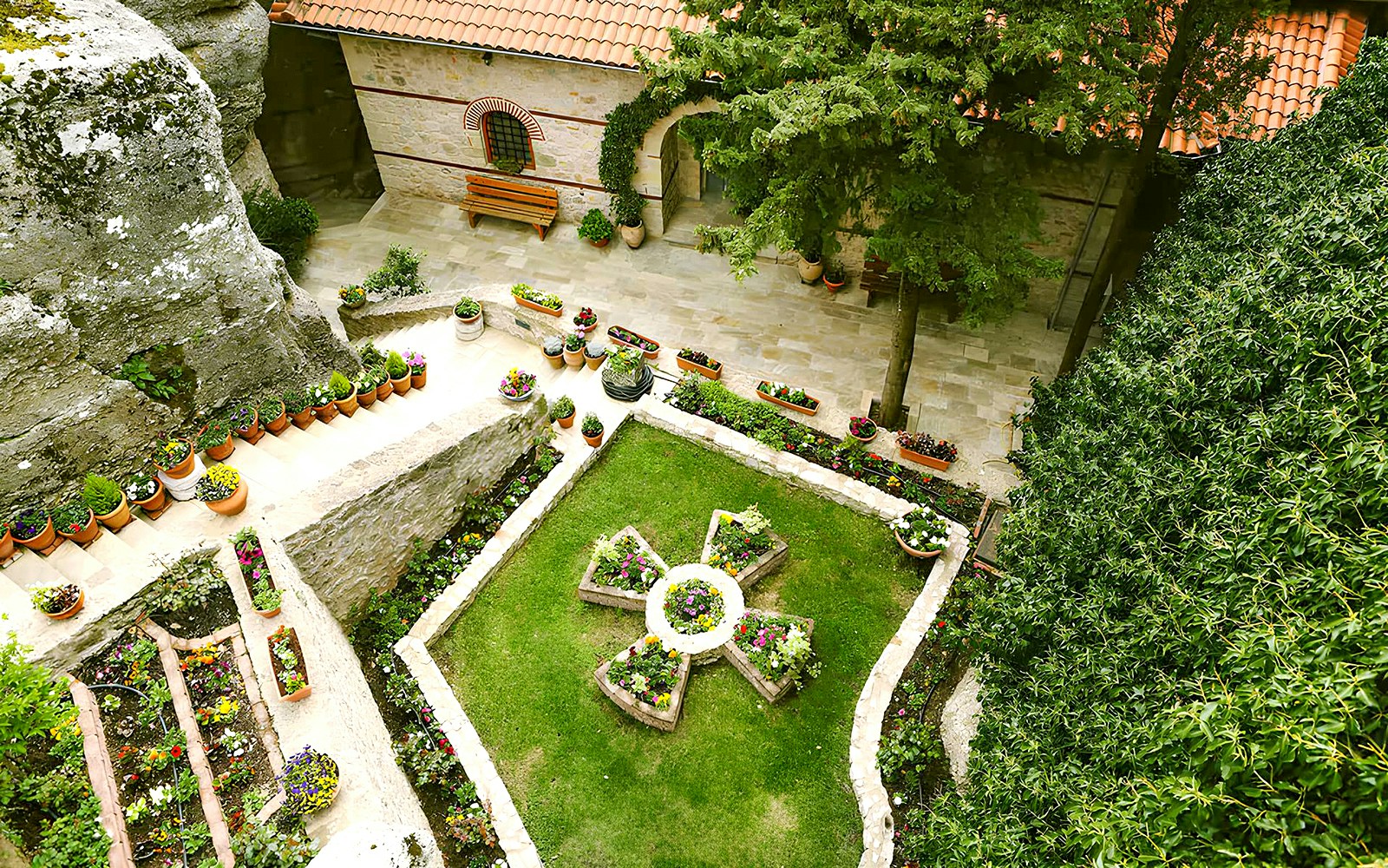 Meteora Monastery garden with stone pathways and lush greenery, Greece.