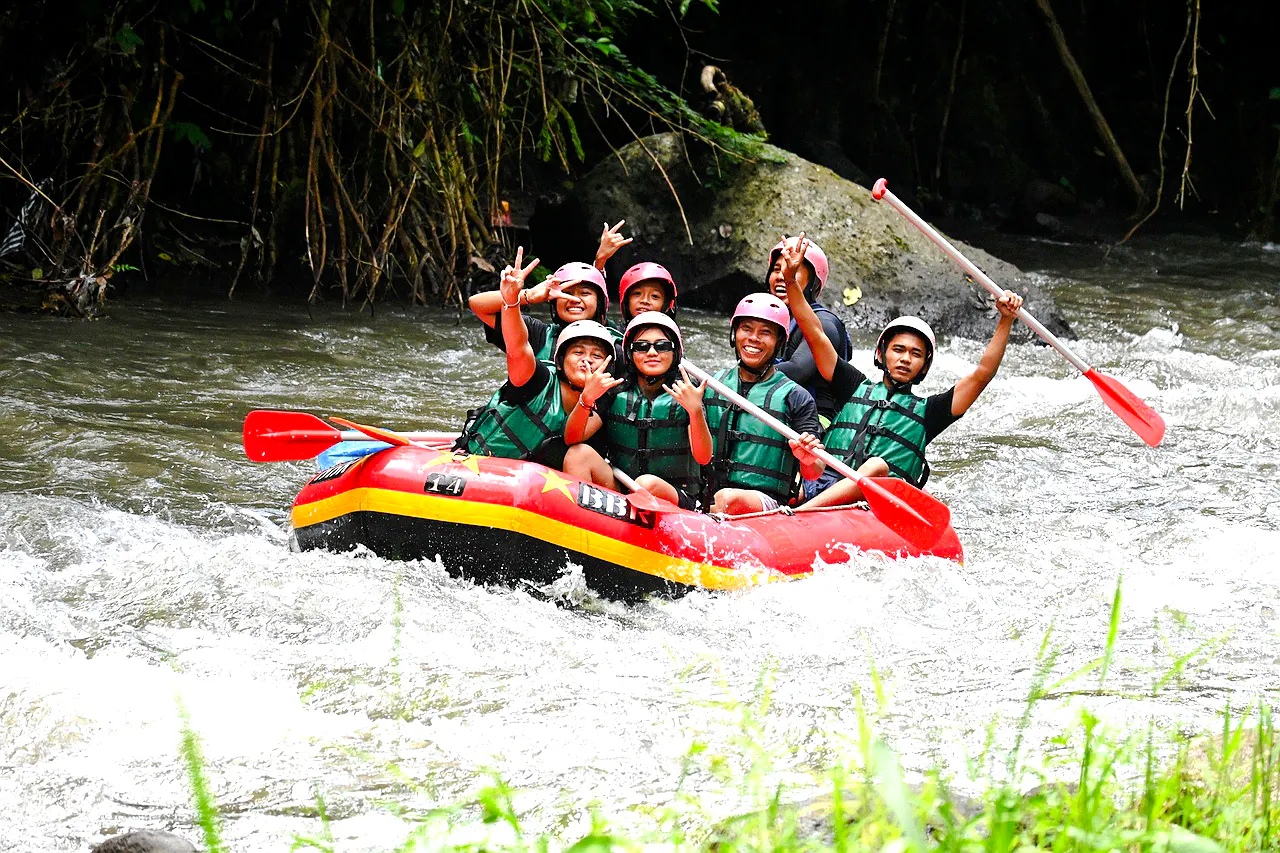 Group rafting on Ayung River, Bali, with paddles raised, surrounded by lush greenery.
