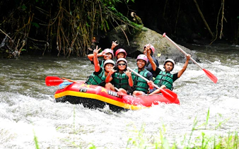 Group rafting on Ayung River, Bali, with paddles raised, surrounded by lush greenery.