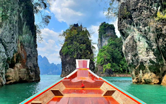 Boat navigating between limestone cliffs on Cheow Lan Lake, Krabi.
