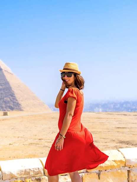 Tourist in red dress posing in front of Pyramids of Giza, Egypt.